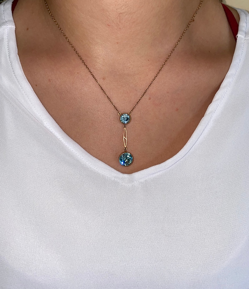 Op de afbeelding: Een gouden ketting met een delicaat hangertje met twee ronde blauwe edelstenen.