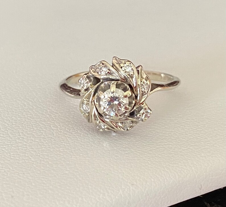 Puede incluir: Un anillo de plata con un gran diamante redondo en el centro, rodeado de diamantes m&aacute;s peque&ntilde;os engastados en un dise&ntilde;o floral.