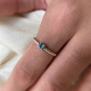 May include: A silver ring with a blue gemstone set in a twisted band.