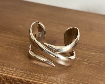 May include: A silver cuff bracelet with a unique, abstract design. The bracelet is made of two curved pieces of metal that are joined together at the ends.