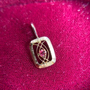 May include: A gold pendant with a pink gemstone set in a geometric design.