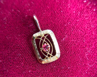 May include: A gold pendant with a pink gemstone set in a geometric design.