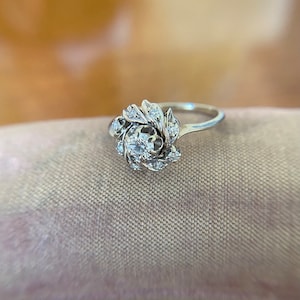 Puede incluir: Un anillo de plata con un grupo de peque&ntilde;os diamantes engastados en un dise&ntilde;o floral.