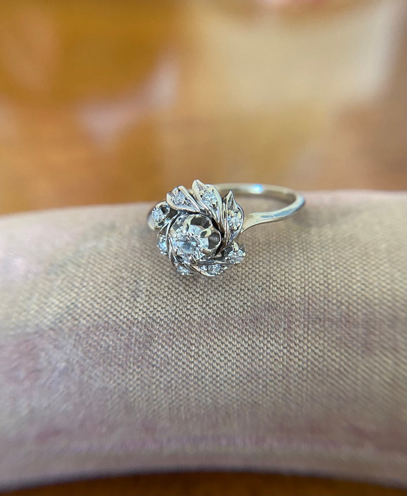 Puede incluir: Un anillo de plata con un grupo de peque&ntilde;os diamantes engastados en un dise&ntilde;o floral.