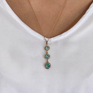 Op de afbeelding: Een gouden ketting met een hanger met drie ronde blauwe edelstenen.