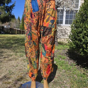 May include: Patchwork pants with an elastic waistband and drawstring. The pants feature a variety of colorful fabric patches in shades of orange, yellow, green, and blue. The pants have a relaxed fit and are cuffed at the ankles.