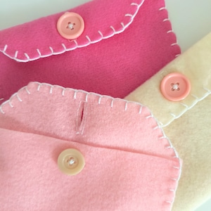 May include: Three felt envelopes with white stitching and pink, cream, and light pink buttons.