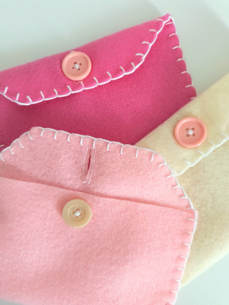 May include: Three felt envelopes with white stitching and pink, cream, and light pink buttons.