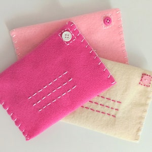 May include: Three felt envelopes in pink, light pink, and cream with white and pink stitching. Each envelope has a button closure.