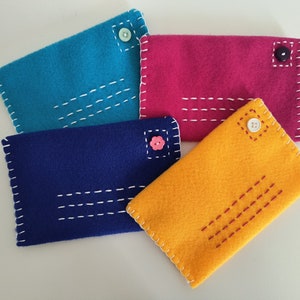 May include: Four felt envelopes with different colored buttons. The envelopes are turquoise, pink, blue, and yellow. The envelopes have white stitching around the edges and white stitching across the front.