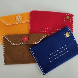 May include: Four felt fabric envelopes with different colored felt and buttons. The envelopes are stacked on top of each other. The top envelope is red, the second is brown, the third is yellow, and the bottom envelope is blue.
