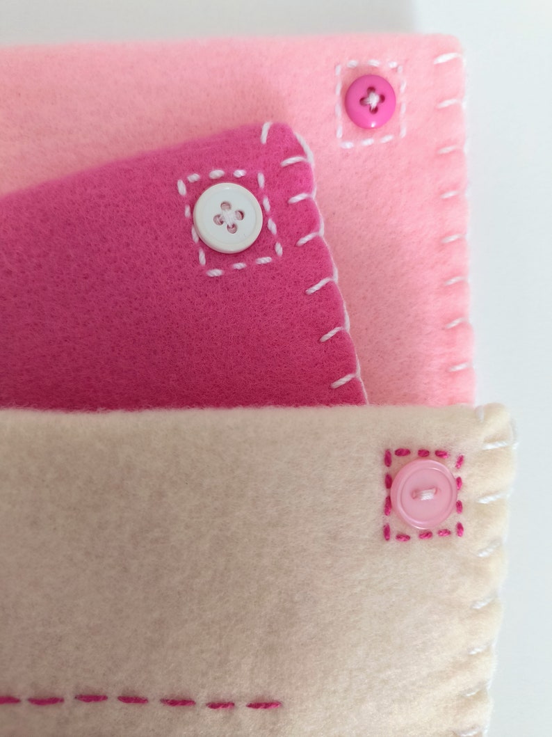 May include: Three layers of fabric in pink, light pink, and cream colors, each with a button sewn on. The buttons are white, pink, and pink. The fabric is stitched with pink thread.