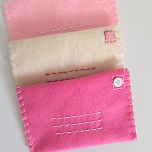 May include: Three felt envelopes in pink, cream, and hot pink with white stitching and pink buttons.