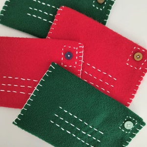 May include: Four felt envelopes in green and red with white stitching and different colored buttons. The envelopes are stacked on top of each other.