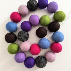 May include: A garland of colorful felt balls in shades of pink, purple, blue, green, and brown. The balls are strung together on a white string, creating a decorative element. The felt balls are approximately 1 inch in diameter.