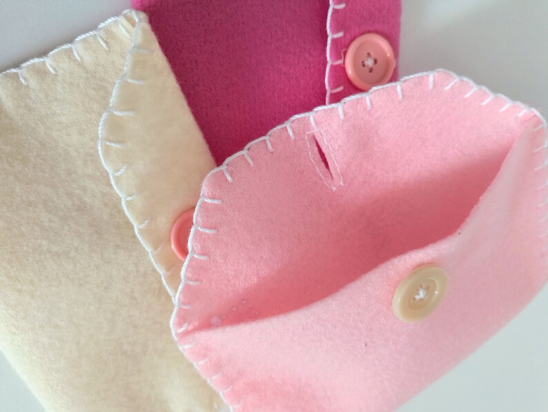 May include: Three felt pouches with white stitching and button closures. The pouches are in shades of pink and cream.
