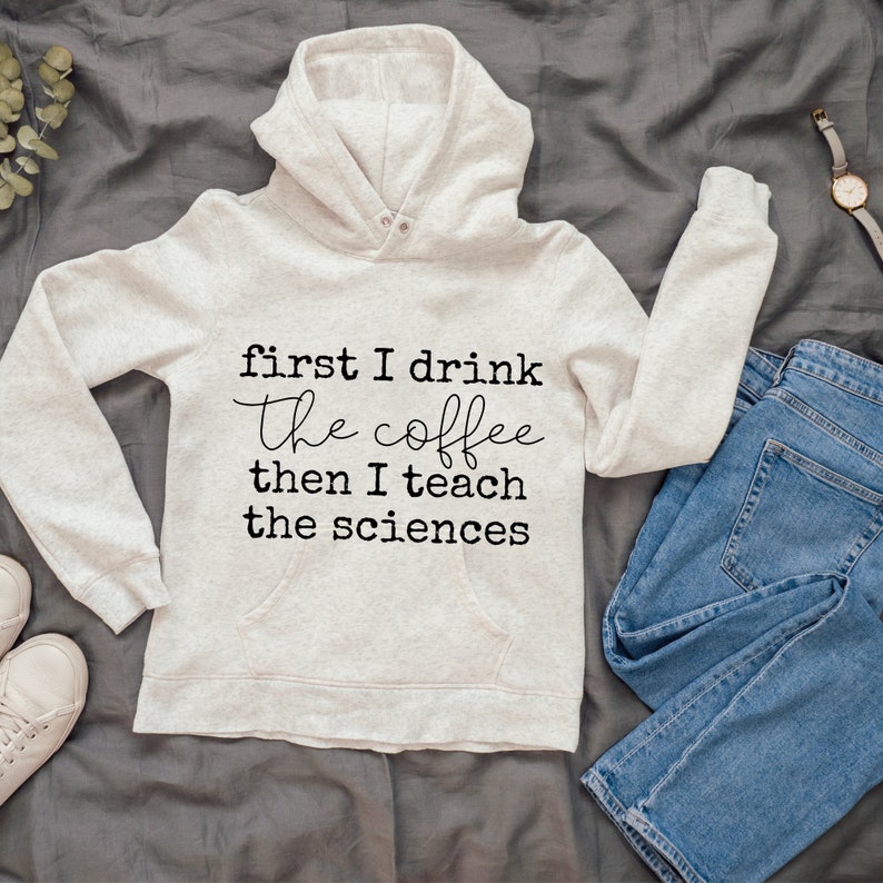 May include: A light gray hoodie with a black graphic that reads "first I drink the coffee then I teach the sciences".