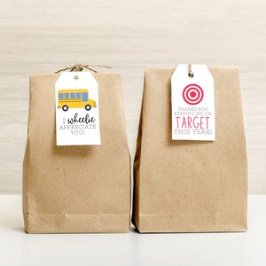 May include: Two brown paper bags with gift tags. The tag on the left bag has a yellow school bus illustration and the text "I wheellie appreciate you!" The tag on the right bag has a red target symbol and the text "Thanks for keeping me on target this year!"
