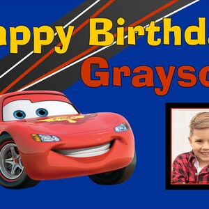 May include: A red race car with a number 95 on the side, a smiling face, and blue eyes. The car is on a blue background with black and red stripes. The text "Happy Birthday Grayson" is in yellow and red letters. A photo of a young boy is in a frame on the right side of the image.