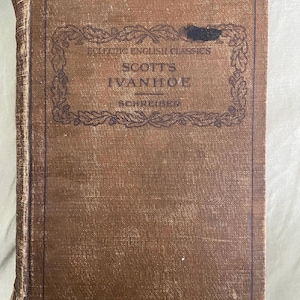 May include: A vintage hardcover book with a brown cover. The title "SCOTT'S IVANHOE" is visible, along with the text "ECLECTIC ENGLISH CLASSICS" and "SCHREIBER" in a decorative frame. The book shows signs of wear.