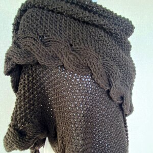 May include: A brown knitted shawl with a cable knit pattern. The shawl is draped over a mannequin.
