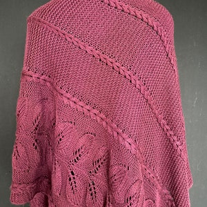 Könnte beinhalten: Ein maronenfarbener Strick-Schal mit einem zarten Spitzenmuster. Der Schal ist über eine Schaufensterpuppe drapiert und hat eine weiche, fließende Textur.