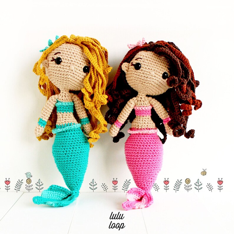 Peut inclure: Deux poup&eacute;es sir&egrave;nes en crochet avec de longs cheveux boucl&eacute;s. Une poup&eacute;e a une queue turquoise et l'autre une queue rose. Les deux poup&eacute;es ont les yeux bruns et portent un haut en crochet.