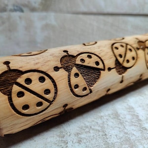 May include: A wooden rolling pin with a design of ladybugs engraved into the surface. The ladybugs are brown and have black spots.