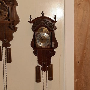 Może przedstawiać: Dwa antyczne drewniane zegary z ozdobnymi rzeźbami i złotymi akcentami. Każdy zegar ma wahadło i tarczę z cyframi rzymskimi.