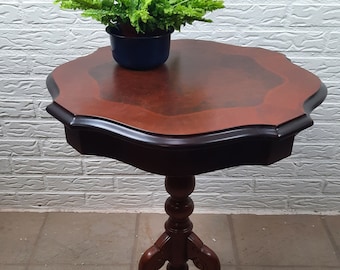 Op de afbeelding: Een donkerhouten bijzettafel met een gegolfd blad en drie poten. Een groene plant in een blauwe pot staat op de tafel.
