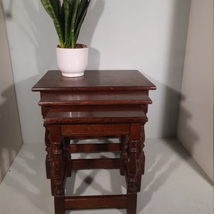 May include: A set of three wooden nesting tables with turned legs. The tables are made of dark wood and have a simple, classic design. A potted plant sits on top of the largest table.