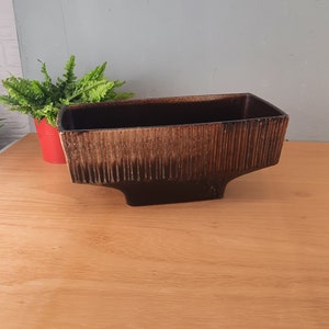 Könnte beinhalten: Ein brauner und schwarzer Keramik-Pflanztopf mit rechteckiger Form und einer strukturierten Oberfläche. Der Topf hat eine breite Basis und eine schmale Oberseite.