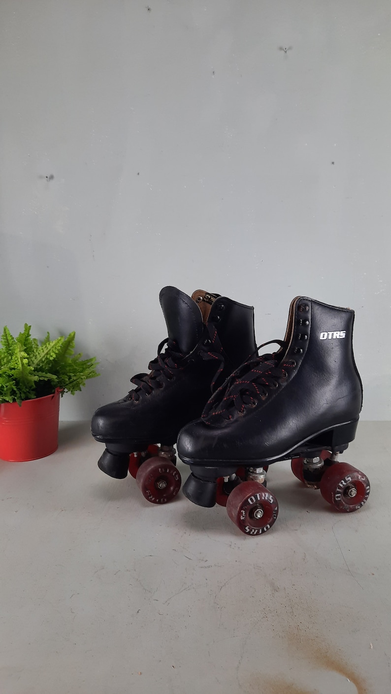May include: A pair of black roller skates with red wheels. The wheels have the word "OTRS" printed on them.