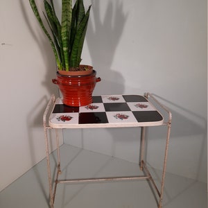 May include: A white metal side table with a black and white checkered top. The table has a red ceramic planter with a green snake plant on top.