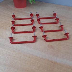 Könnte beinhalten: Acht rote Schranktürgriffe mit silbernen Schrauben. Die Griffe liegen in einer Reihe auf einer hellbraunen Holzoberfläche.