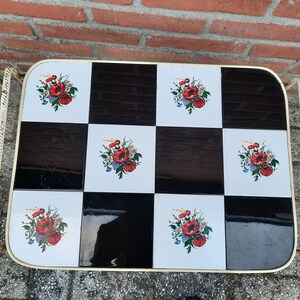 May include: A white metal serving cart with a black and white checkered top. The top is decorated with red and white floral designs.