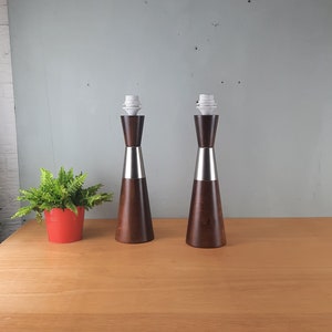 May include: Two brown and silver table lamps with white lampshades. The lamps are on a wooden table.