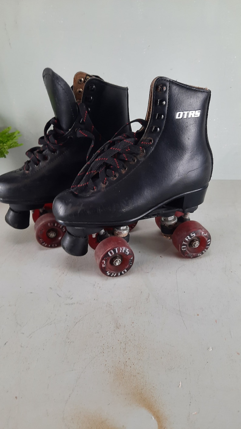 May include: A pair of black roller skates with red wheels. The skates have black laces and the word "OTRS" is printed on the side of the right skate.