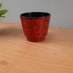 May include: A red and black ceramic planter with a speckled glaze. The planter has a rounded shape and a black rim.