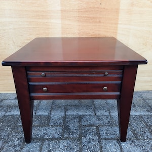 Könnte beinhalten: Ein dunkler Holz-Beistelltisch mit zwei Schubladen und einer glatten, polierten Oberfläche. Der Tisch hat eine rechteckige Tischplatte und vier Beine.