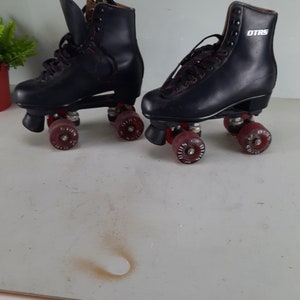 May include: A pair of black roller skates with red wheels. The skates have black leather boots with laces and the text "OTRS" on the side of the right skate.