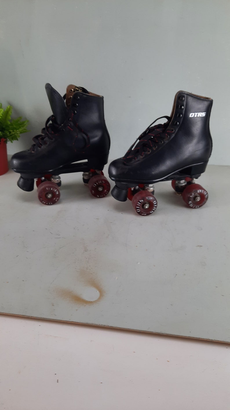 May include: A pair of black roller skates with red wheels. The skates have black leather boots with laces and the text "OTRS" on the side of the right skate.
