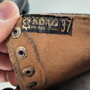 May include: Close-up of a brown leather boot with a black label that reads "AGRO PROFESSIONAL 37".