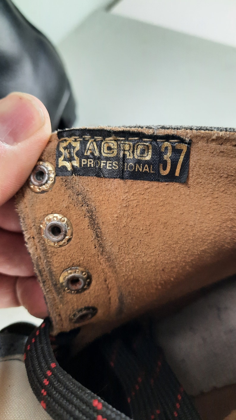 May include: Close-up of a brown leather boot with a black label that reads "AGRO PROFESSIONAL 37".