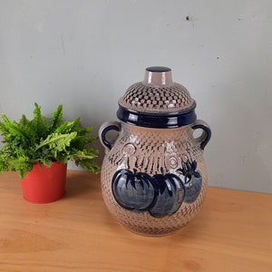 Op de afbeelding: Een keramische pot met een blauw en wit ontwerp met tomaten. De pot heeft een deksel met een geruit patroon en twee handvatten.