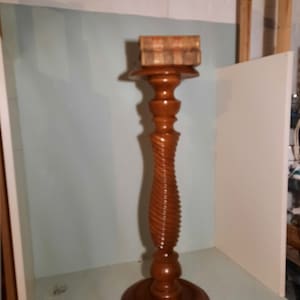 Op de afbeelding: Een houten voetstuk met een gedraaide kolom en een ronde bovenkant. Een boek ligt op de bovenkant van het voetstuk.