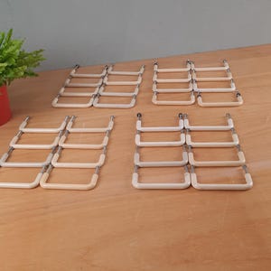 Op de afbeelding: Een set van 18 witte kunststof ladegrepen met zilveren metalen accenten. De grepen zijn gerangschikt in drie rijen van zes op een houten oppervlak.