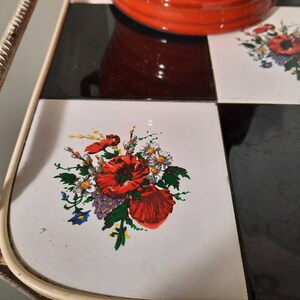 May include: A white metal serving tray with a black and white checkered pattern. The tray has a floral design with red poppies and white daisies on one of the tiles.