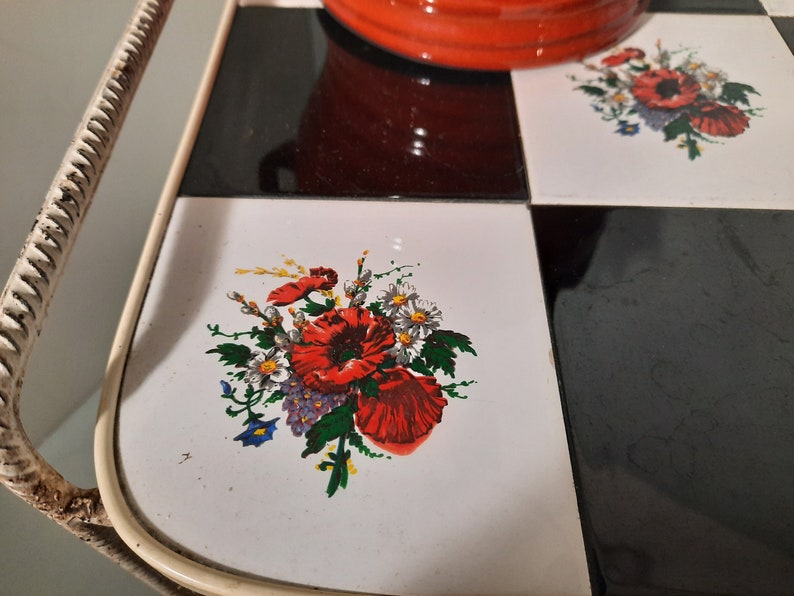 May include: A white metal serving tray with a black and white checkered pattern. The tray has a floral design with red poppies and white daisies on one of the tiles.