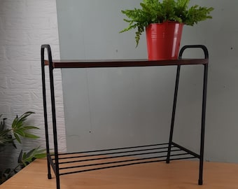 May include: A black metal plant stand with a dark brown wooden shelf and a lower rack. A red pot with a green plant sits on the shelf. The stand has a minimalist design and is suitable for indoor use.